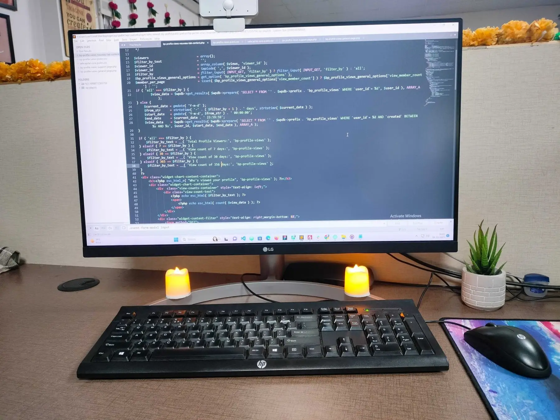 A desk with code on a monitor, candles and a small plant